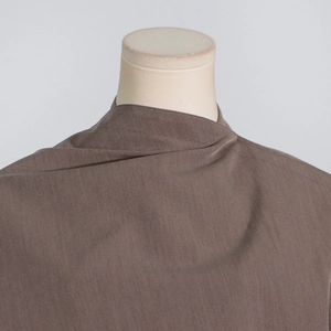 Detailed close-up of brown blazer neckline with asymmetric fold design and smooth texture