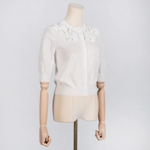 Detail of white knit cardigan showing elegant 3D floral accents on the shoulder