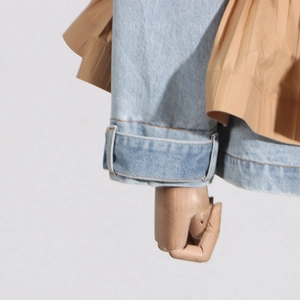 Detailed view of light blue denim fabric with khaki pleated satin contrast and stitching