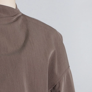 Macro view of dark brown suit jacket featuring high mock neck and detailed shoulder seams
