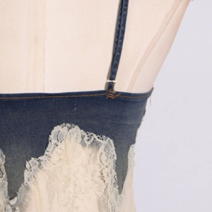Close-up of denim bodice with yellow stitching and white lace patchwork detail