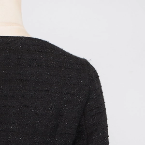 Close-up of black tweed dress fabric with shimmering sequins and shoulder seam detail