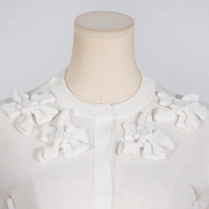 Detail of white knit cardigan showing 3D floral appliques and polished buttons on shoulders