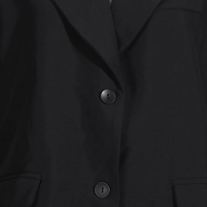 Détail de blazer noir avec col à revers, fermeture à deux boutons et poches à rabat