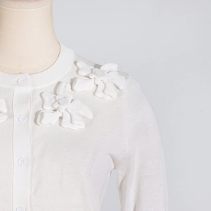 Detail of 3D floral appliqué on white knit cardigan with textured fabric and buttons