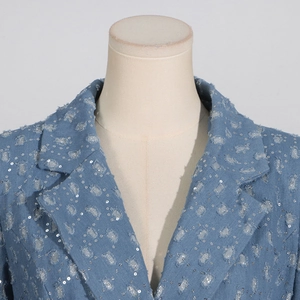 Détail d'un trench-coat en jean bleu clair avec paillettes argentées et détails de franges