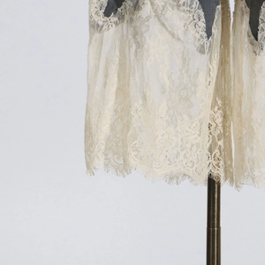 Close-up of beige floral eyelash lace hem detail on a dark grey fabric background