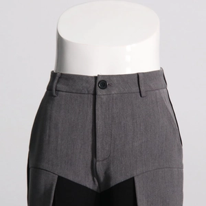 Detail of grey casual pants featuring black patchwork and a single button waist closure