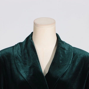 Detail view of dark green velvet blazer fabric with large lapel on a beige mannequin