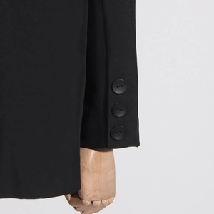 Détail du poignet d'un blazer noir déconstruit avec trois boutons décoratifs noirs