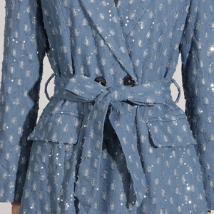 Détail du trench-coat en jean à paillettes bleues avec bords effilochés et boutons croisés