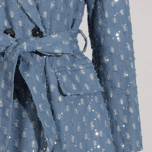 Détail d'un trench en denim bleu clair à paillettes avec ceinture et boutons à double boutonnage