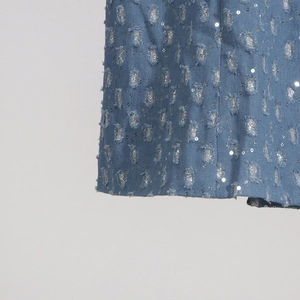 Détail du tissu denim bleu clair avec des trous usés et des paillettes argentées