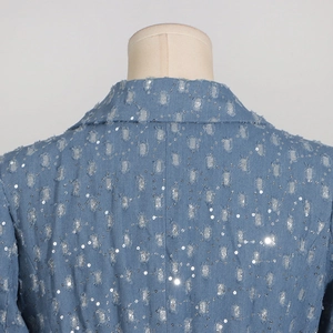 Gros plan détaillé du trench-coat en jean bleu clair avec sequins argentés et détails usés