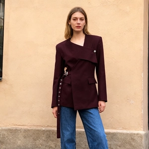 Detail of burgundy blazer showing asymmetric lapel and belted waist with metal eyelets