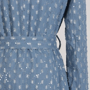 Détail du tissu denim bleu clair avec paillettes argentées et franges vieillies