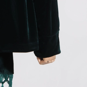 Detailed close-up of dark green velvet sleeve cuffs and fine fringe tassel hemline