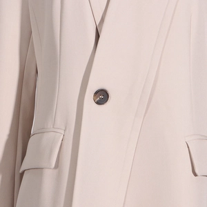 Detail of beige trench coat featuring lapel collar and amber texture button close-up