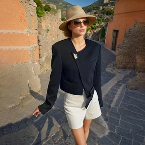 Detail of a black blazer with an asymmetric front, metal brooch, and matching waist belt