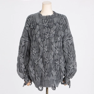 Detail of grey cable-knit texture and distressed ripped edges on a loose-fit sweater