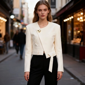 Detail of white blazer featuring asymmetric collar and gold heart-shaped brooch accent