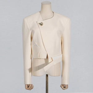 Close-up of asymmetrical off-white blazer featuring a gold shell brooch and geometric hem