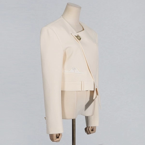 Detail view of beige blazer with asymmetrical closure and golden fan-shaped button