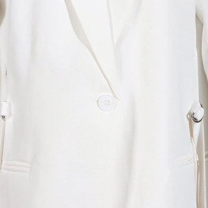 Détail d'un blazer blanc avec revers et sangle latérale réglable à anneau métal