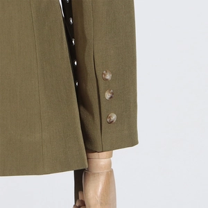 Detail of olive green blazer sleeve with amber buttons and metal eyelet ribbon trim