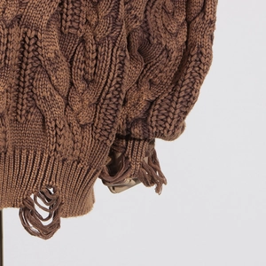 Close-up of brown chunky knit sweater showing detailed cable texture and distressed hem