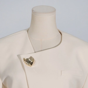 Detail of cream blazer with asymmetric lapel and golden seashell brooch decoration