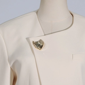 Detailed view of a wavy gold-plated brooch pinned on a beige blazer collar