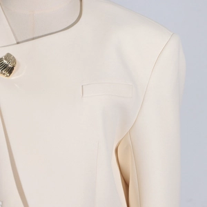 Close-up of a cream blazer featuring a unique gold shell-shaped button and pocket detail