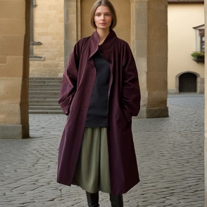 Fashionable dark burgundy trench coat styled with a midi skirt and black boots outdoors