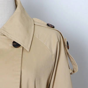 Detailed view of the khaki trench coat featuring shoulder epaulettes and tortoise buttons