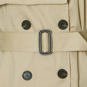 Detail of khaki trench coat featuring double-breasted buttons and a belted waist buckle