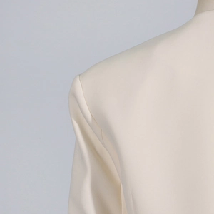 Detail view of cream tailored blazer showing premium fabric texture and fine shoulder stitching