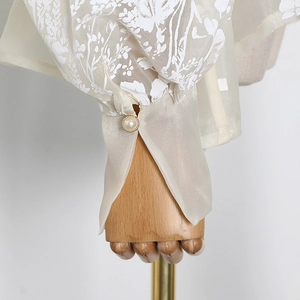 Detail of floral chiffon sleeve with delicate pearl button and elegant gold rim