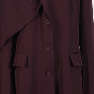 Close-up of asymmetrical draped neckline and buttons on a wine red trench coat