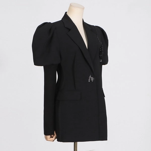 Dettaglio blazer nero con maniche a sbuffo, bottone di paillettes e decorazioni di perline