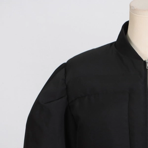 Détail d'une veste noire avec col montant côtelé et manches bouffantes à plis élégants