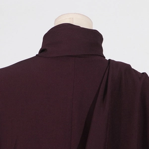 Detailed view of dark burgundy coat featuring a stand collar and elegant shoulder drapes