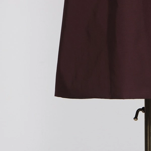 Detailed view of the dark burgundy trench coat fabric hem and smooth woven texture