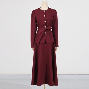 Close-up of wine red top with pearl buttons, round neck tie, and matching bow belt detail