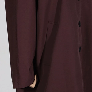 Detail view of coffee brown trench coat featuring black buttons and side pocket stitching