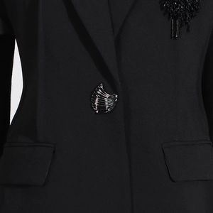 Dettaglio blazer nero con maniche a sbuffo, bottone argentato e toppa floreale con perline