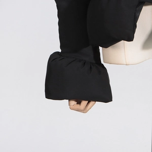 Détail de la manchette de veste noire avec design plissé sur un mannequin en bois