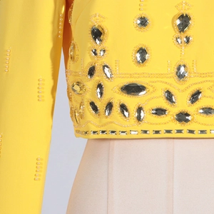 Gros plan d'une broderie lourde avec perles blanches et cristaux sur robe jaune à manches