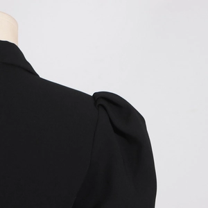 Dettaglio della spalla a sbuffo elegante su un blazer nero con tessuto strutturato