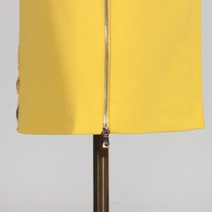 Détail d'une robe jaune avec fermeture éclair dorée et boutons décoratifs en strass